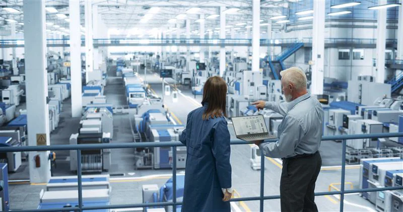 Two engineers standing on a platform looking out at floor with machinery