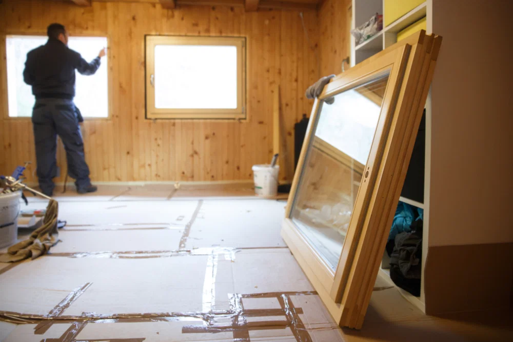 Worker in the backgournd in a Wooden house installing wooden windows for sustainable living & energy savings